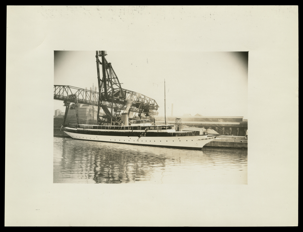 Long boat docked next to an industrial crane or craneway