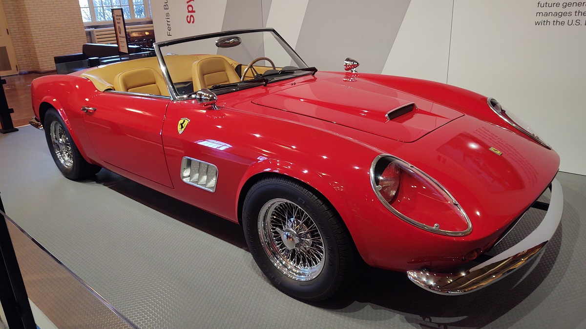 A sleek red convertible with tan interior and top down is parked in a display indoors