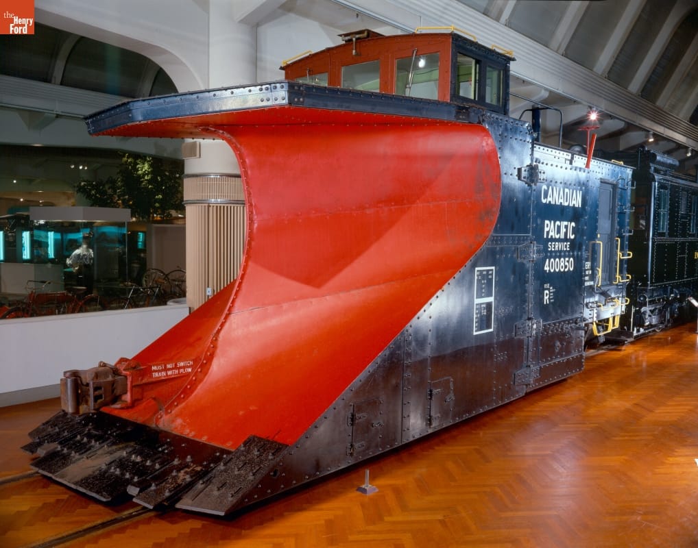 Black railcar with scooped-out front painted red, sitting on tracks in a large room