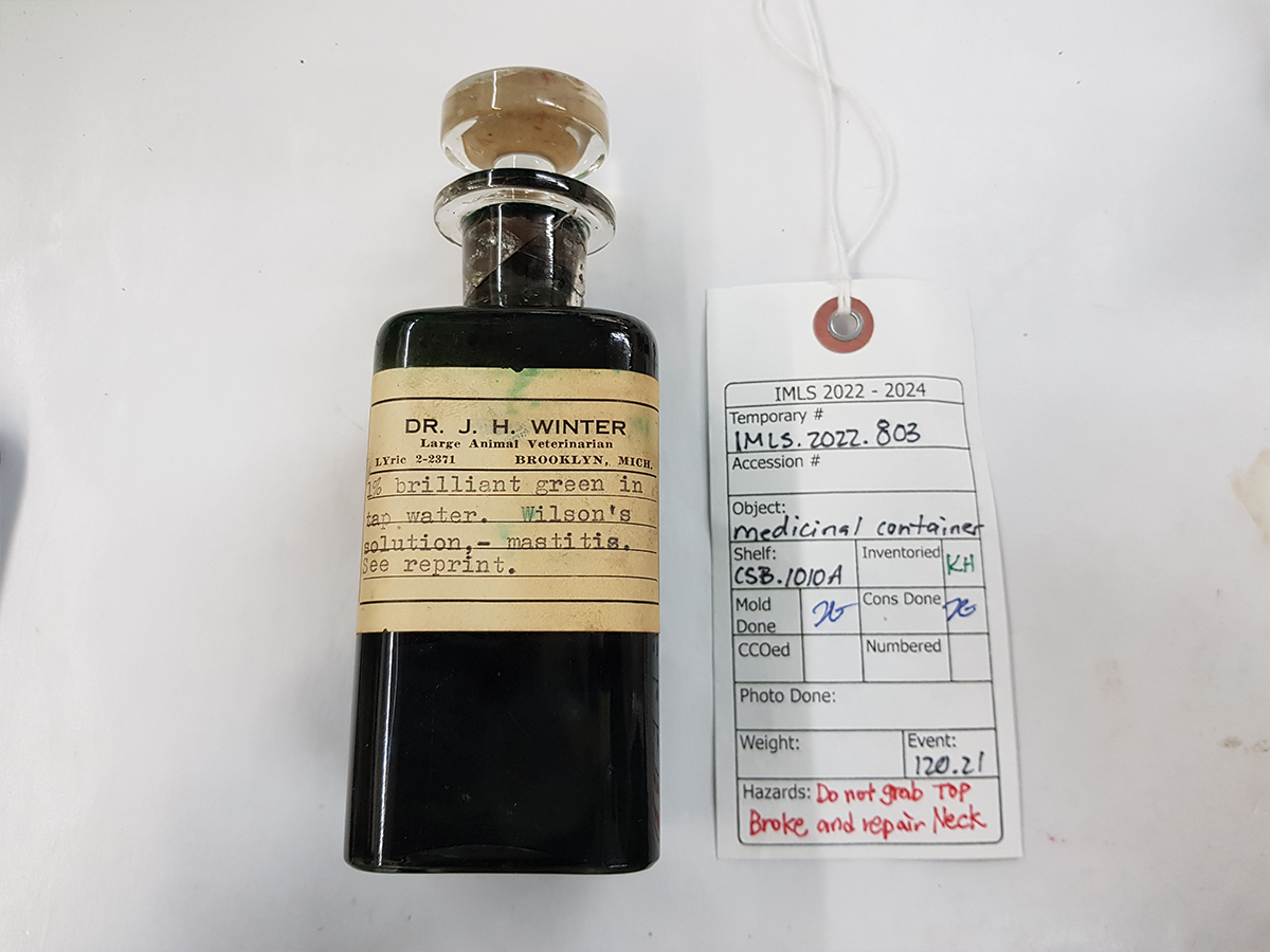 Repaired glass medicinal container with a transparent glass lid was filled with a liquid labelled as ‘1% brilliant green in tap water’.