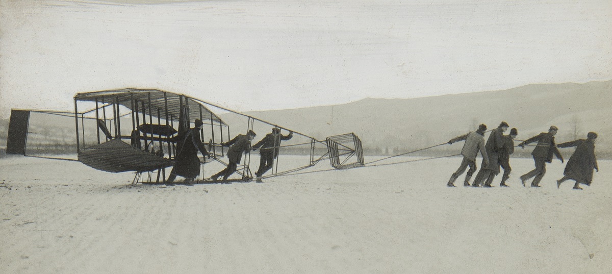 Black-and-white photo of a group of people pulling an early glider across snow or ice