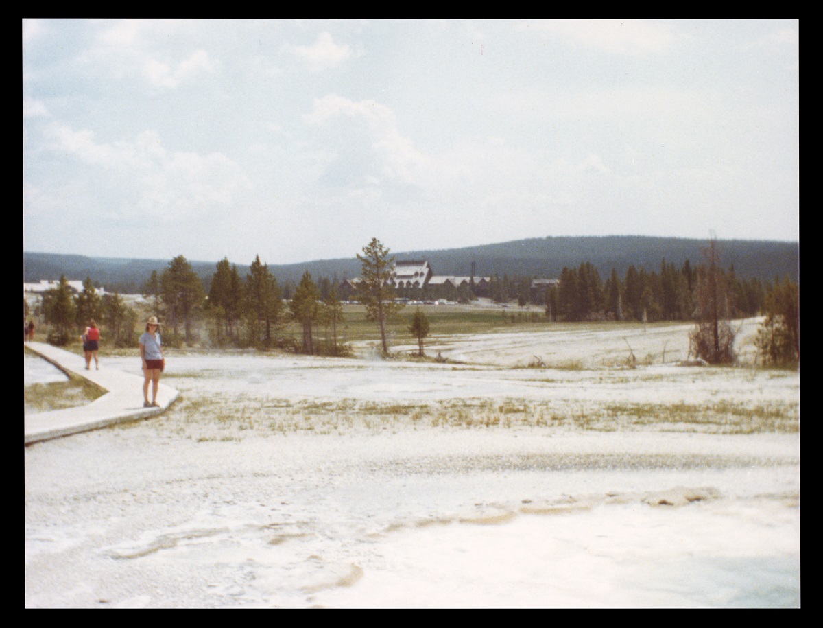 Person stands on boardwalk over white sand or salt with trees and a building in the background
