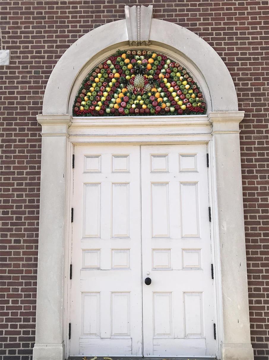 Brick wall with large white double doors topped by an arch of fruit