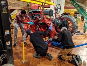 Three men stand and kneel around a piece of equipment, holding a red metal tire