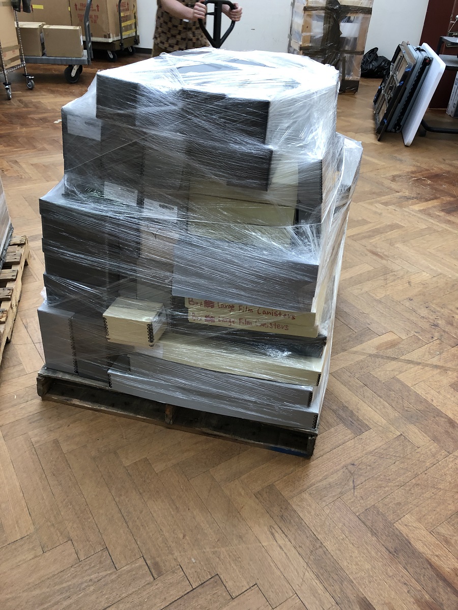 Pallet filled with boxes, all wrapped with clear plastic, sitting in storage area among other boxes and pallets