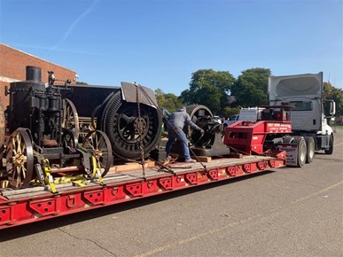 Caravan of large objects being moved out of storage Flatbed semi truck loaded with large machinery and person strapping it down