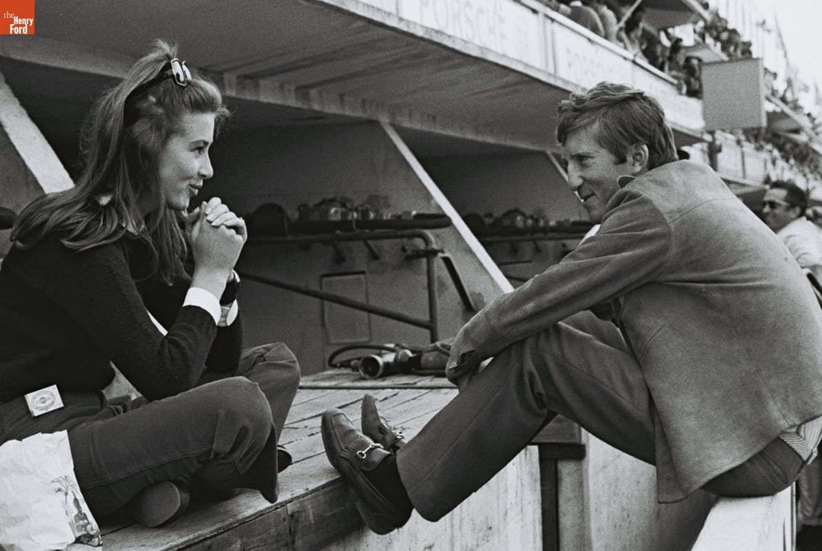 Woman sitting cross-legged smiling at man sitting on low wall with feet extended, also smiling