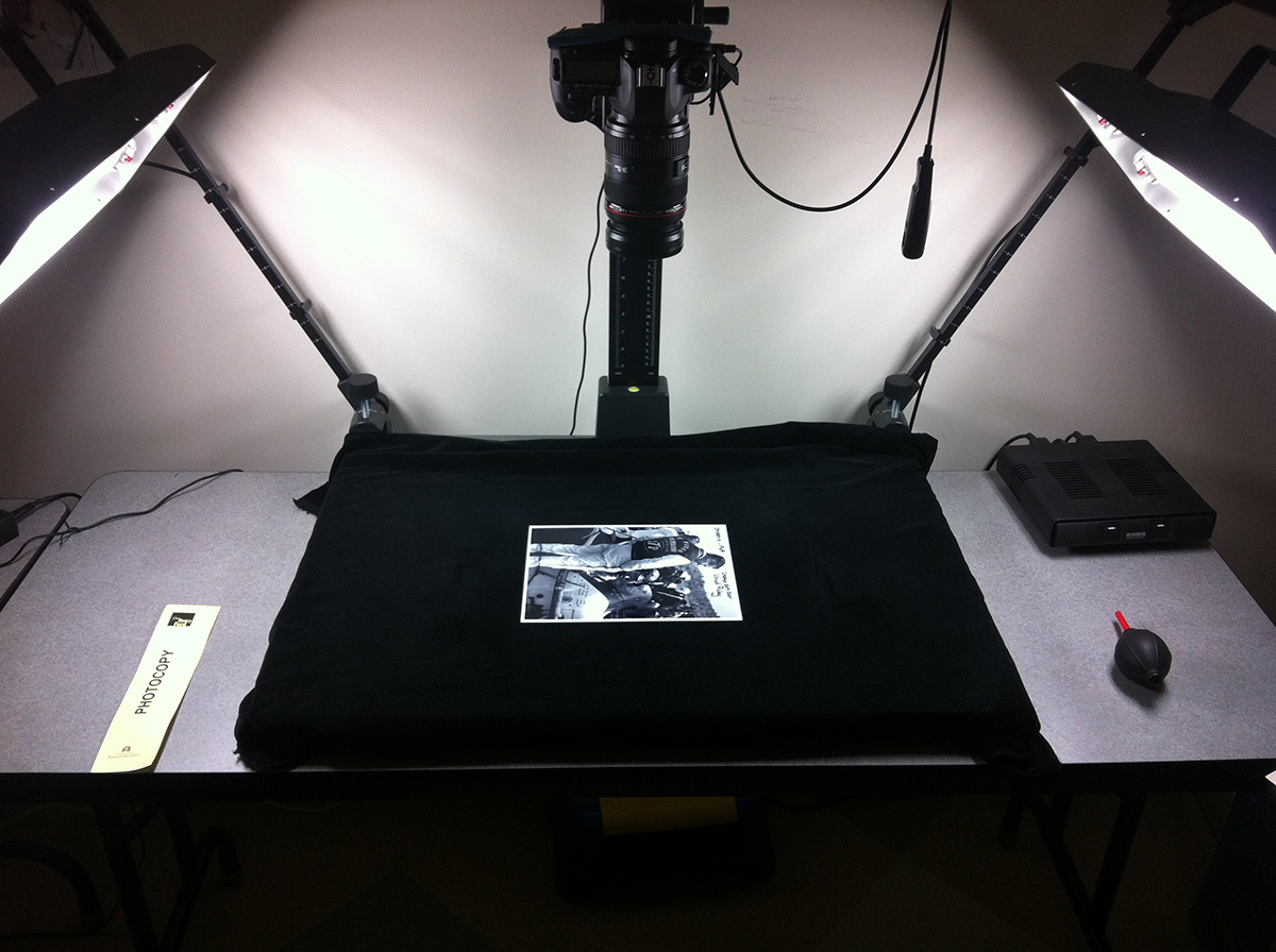 Photograph lying on black fabric with lights on either side and a camera pointed downward at it