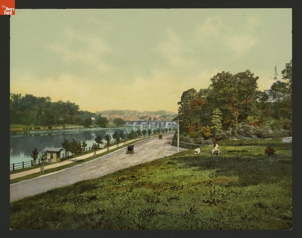 Dirt road along a river, with open lawn and trees on either side