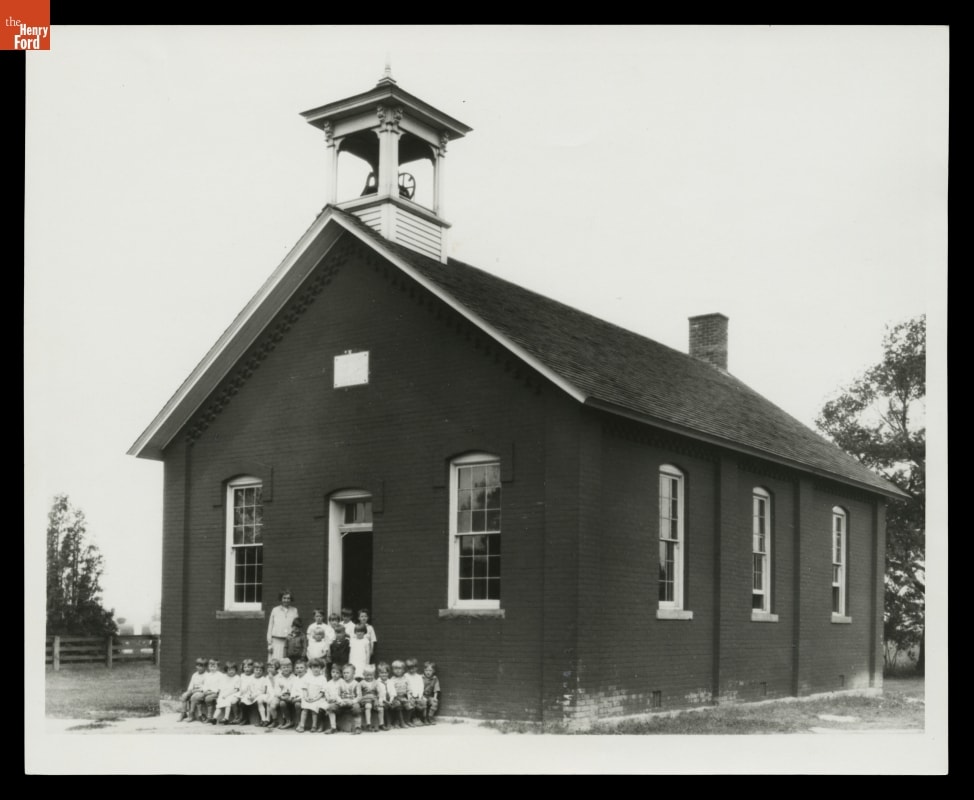 Scotch Settlement School at Its Original Site in Dearborn Township, Michigan, circa 1926 Woman poses for photo with a group of young children outside a small brick building