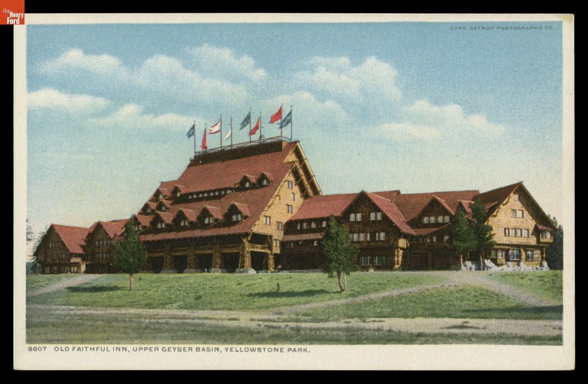 Postcard of sprawling rustic building with steeply peaked roof topped with flags at center; also contains text