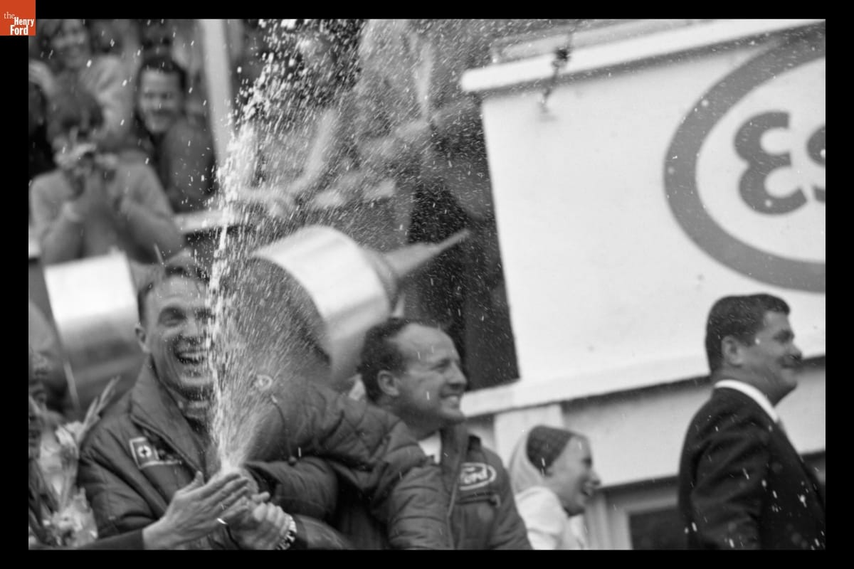 Smiling man sprays champagne from a bottle as others look on