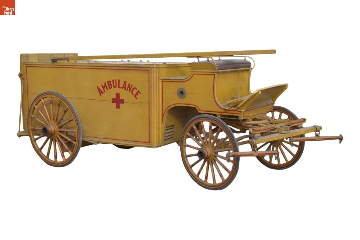 Boxy low yellow wagon with red pinstriping, text "AMBULANCE," and a red cross on the side