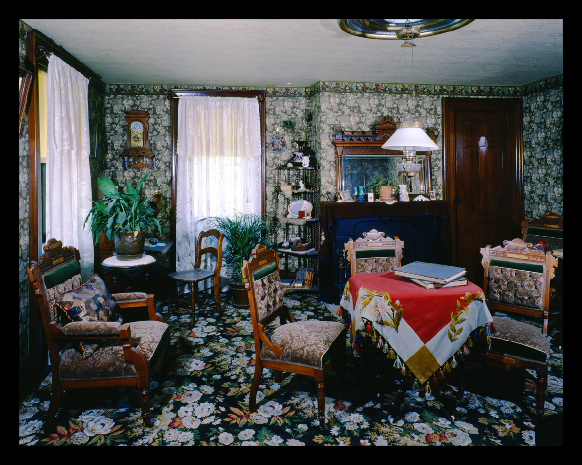Room crowded with furniture and with busy floral carpeting and wallpaper