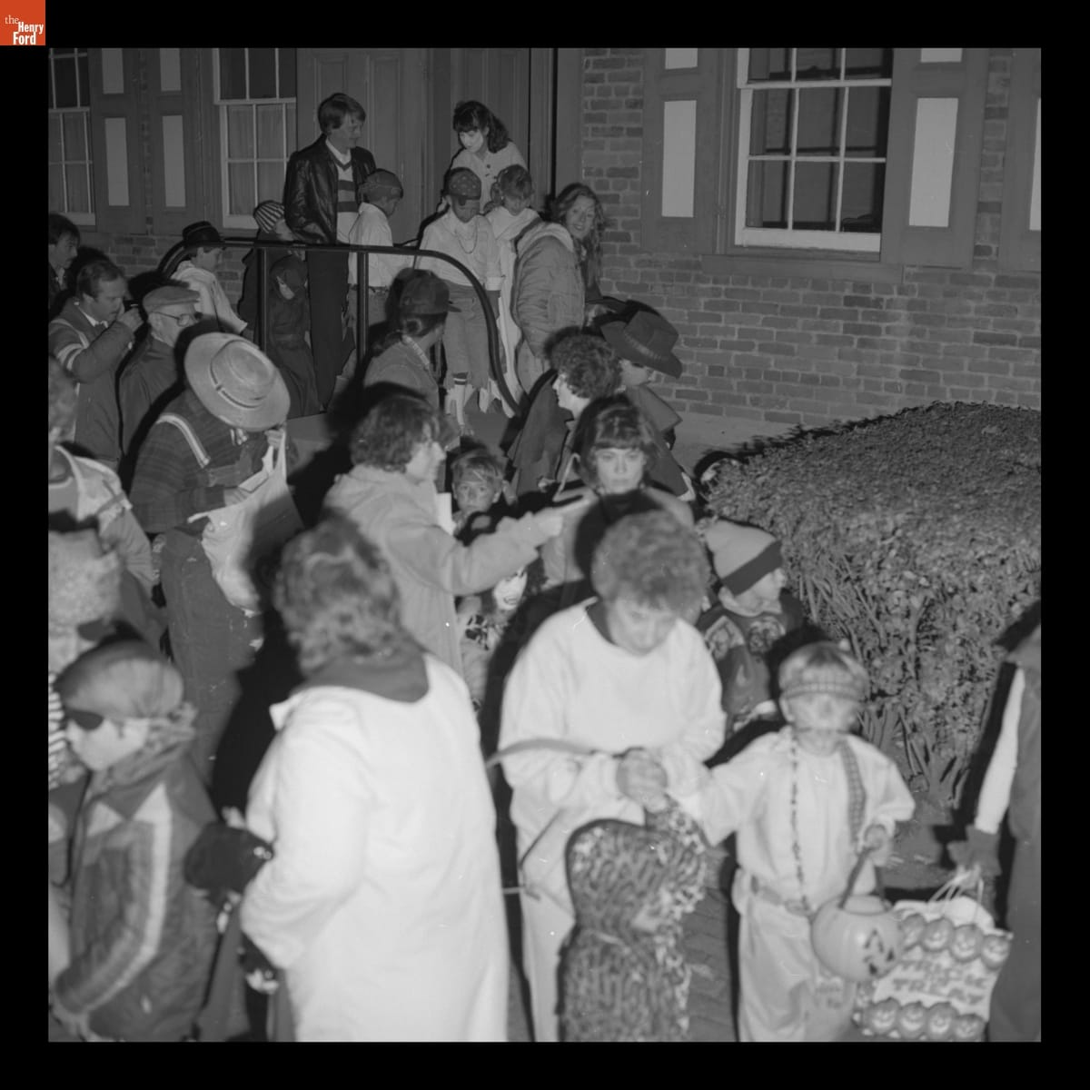"Trick or Treat" at Heinz House in Greenfield Village, October 1982 Crowd of adults and children, many in costume, outside brick house