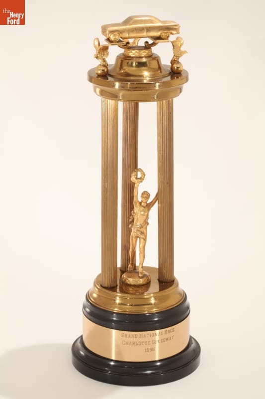 Gold trophy with three tall pillars with car on top; text on black and gold base