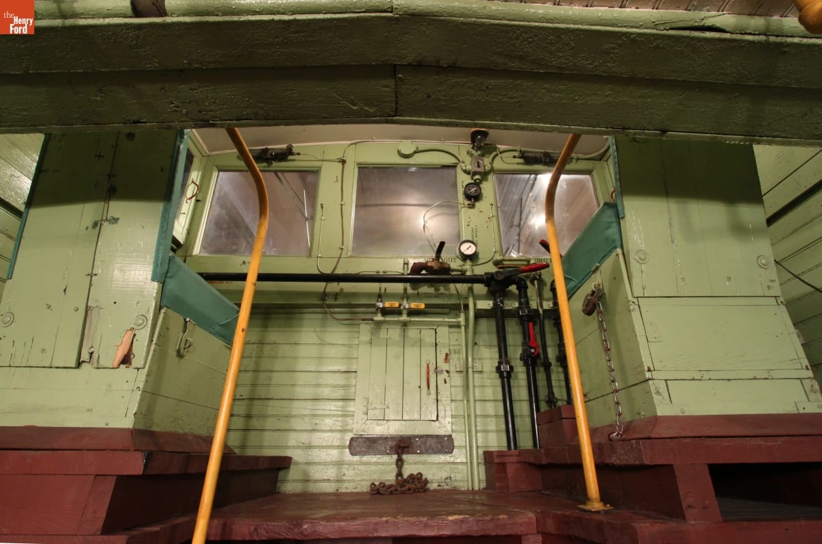 Wooden seats painted green, sitting on wooden platform with equipment and three small windows in front of them 