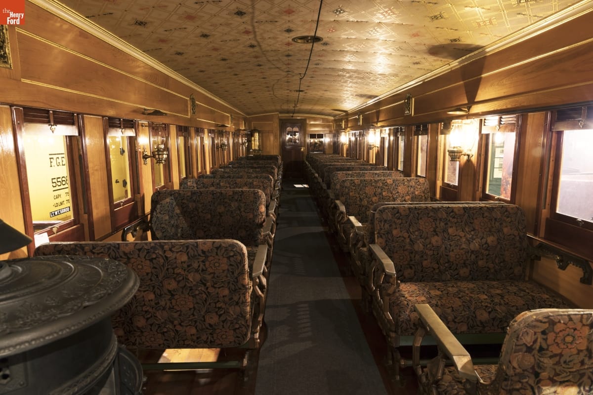 Interior of rail car with floral-upholstered bench seats, wood paneling, and decorative ceiling