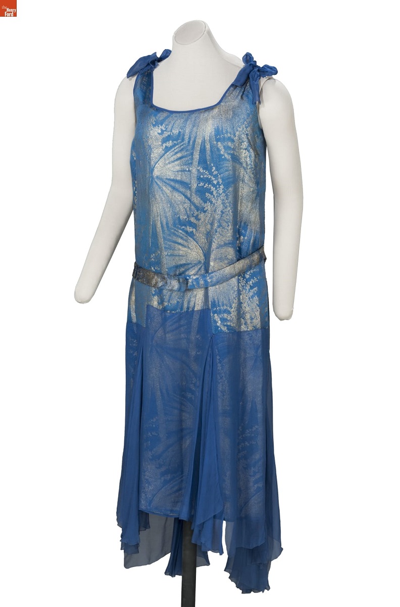 Dress, 1927-1929 Mannequin wearing blue and silver sleeveless drop-waist shift dress with firework- or foliage-patterned top and solid blue handkerchief skirt