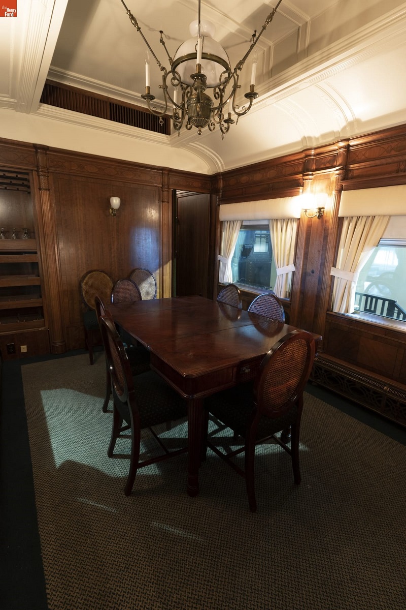 Interior of room with wooden paneling and carpet, containing wooden dining table and chairs