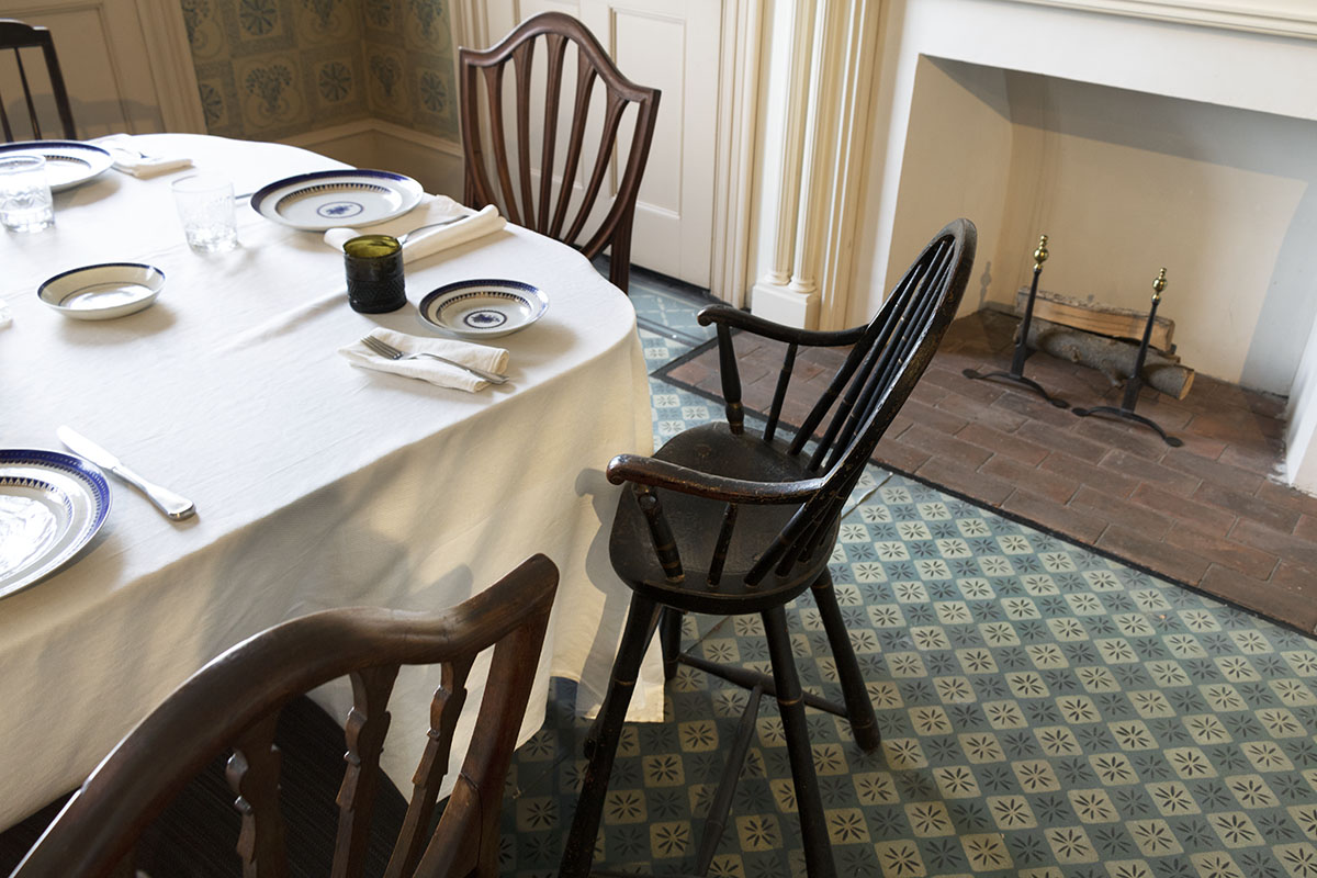 Corner of set table with mismatched chairs; fireplace behind