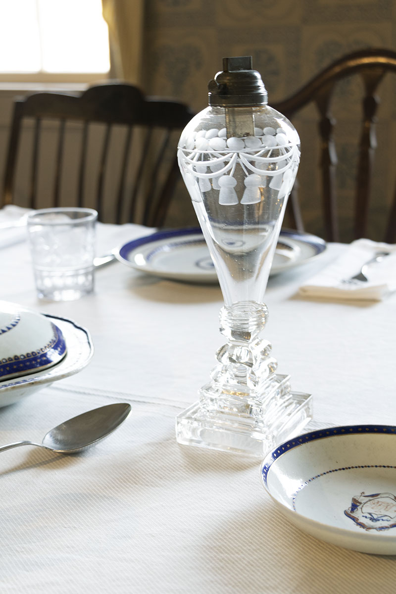 Clear glass lamp with etched pattern on tablecloth with dishes and silverware at place settings nearby