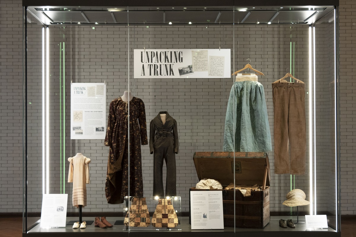 What We Wore: Unpacking a Trunk exhibit in Henry Ford Museum of American Innovation Large glass display case containing a wooden trunk and a number of garments and other pieces of apparel