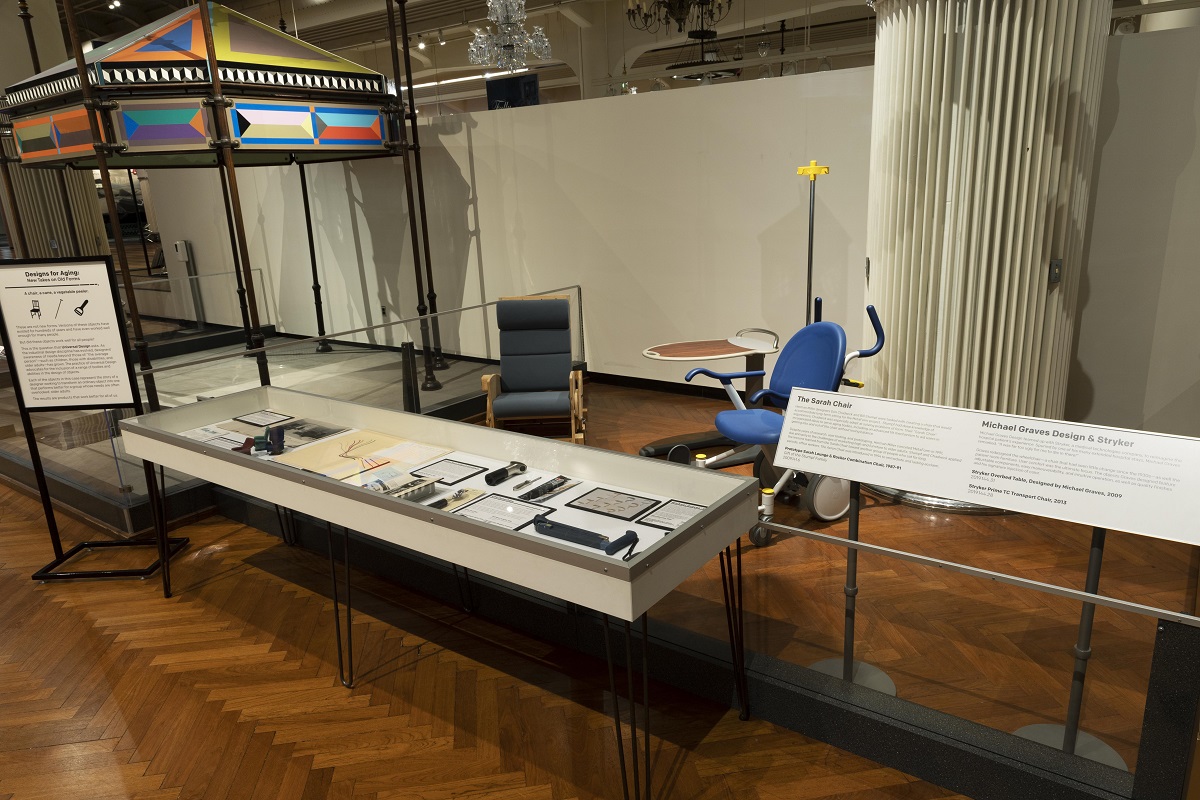 Museum display with large flat case containing paper and small items, a few large artifacts behind it, and extensive labels on either side