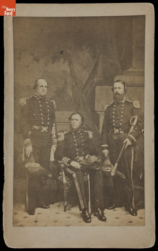 Three men in elaborate uniforms, two standing, one seated