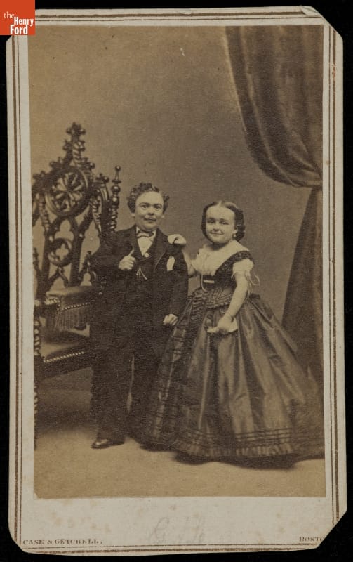 Man and woman in formal suit and dress stand beside large chair