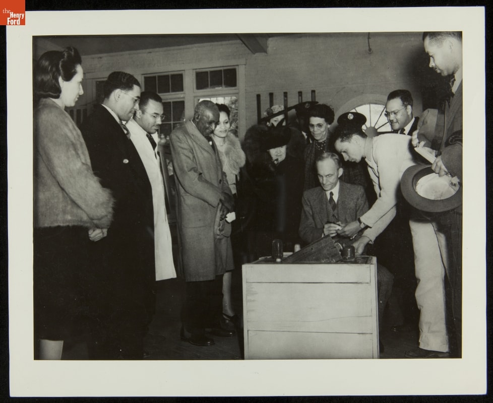 Man sits at crate while other people look on