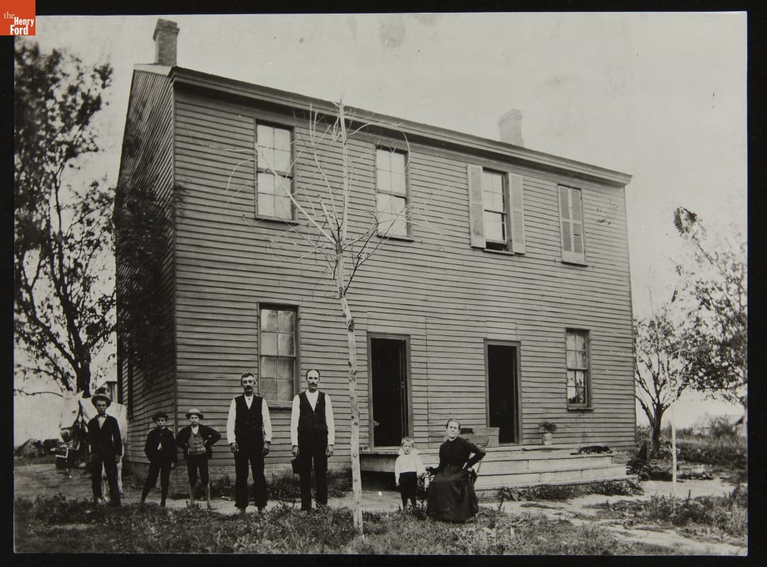 Group outside Logan County Courthouse at Its Original Site, Lincoln, Illinois, circa 1900 Seven children and adults stand and sit outside a two-story wooden building