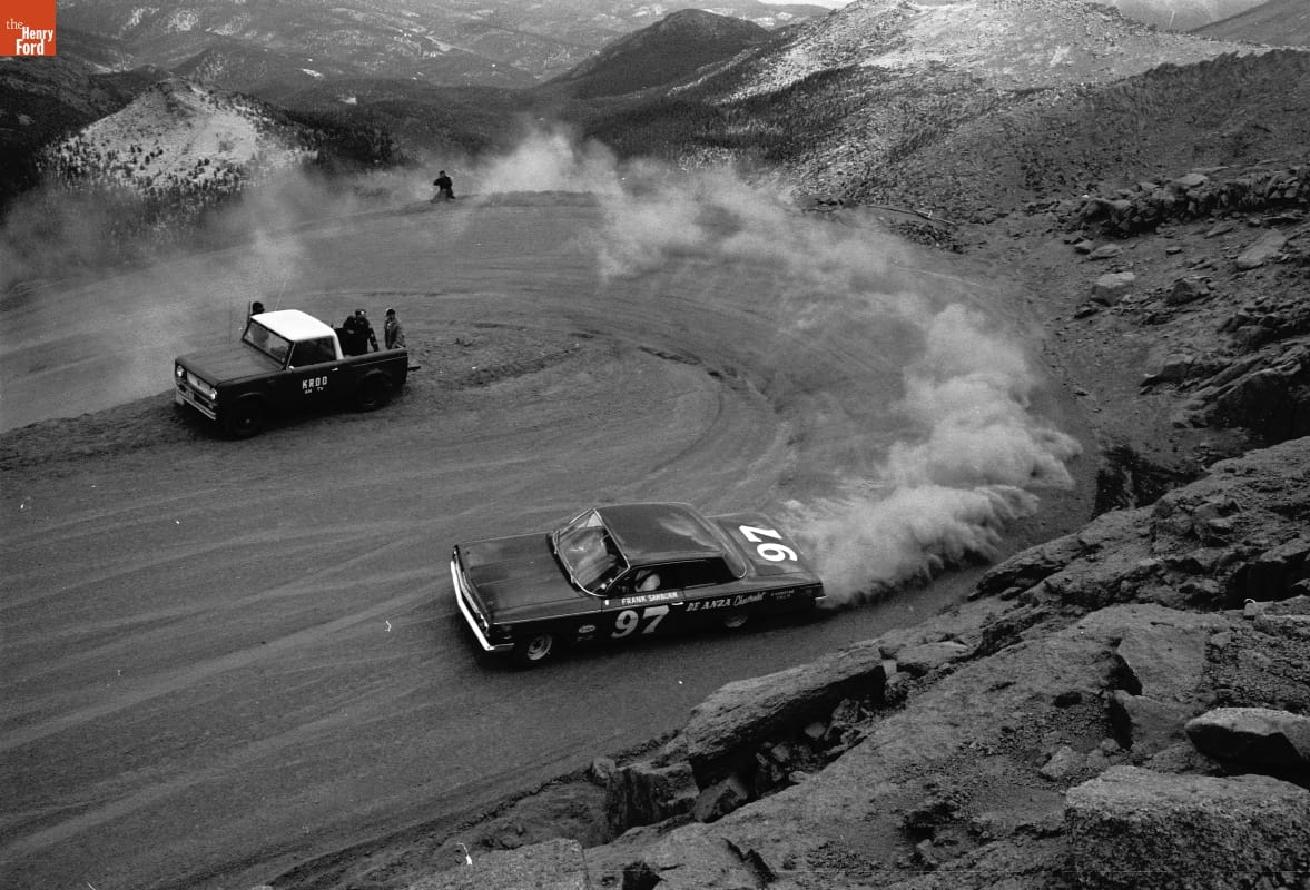 Frank Sanborn Driving Chevrolet Stock Car at Pikes Peak Auto Hill Climb, Colorado Springs, Colorado, July 4, 1962 Car rounding an uphill hairpin curve in a cloud of dust on a dirt road with mountains in the background