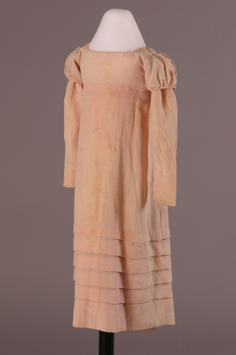 Child's Dress, 1810-1825 Pale pink dress with empire waist; slight puff at top of long sleeves; tiers at bottom of body