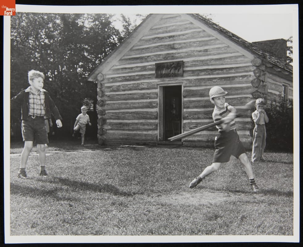 Edison Institute Schoolboys Playing Baseball near McGuffey School, Greenfield Village, September 1940 Four boys stand in front of a log cabin; one swings a bat