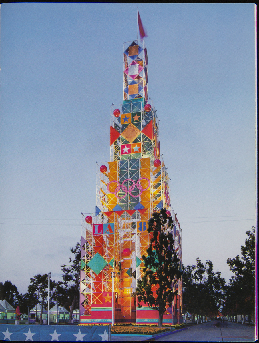 Large colorful tower with decorative scaffolding and images of stars, geometric shapes, and Olympic rings