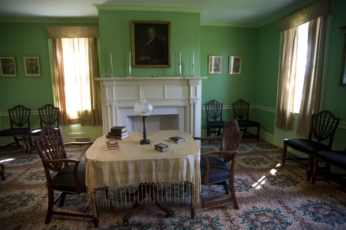 Room with patterned carpet, green walls, table and chairs in middle of room and additional chairs around the perimeter 