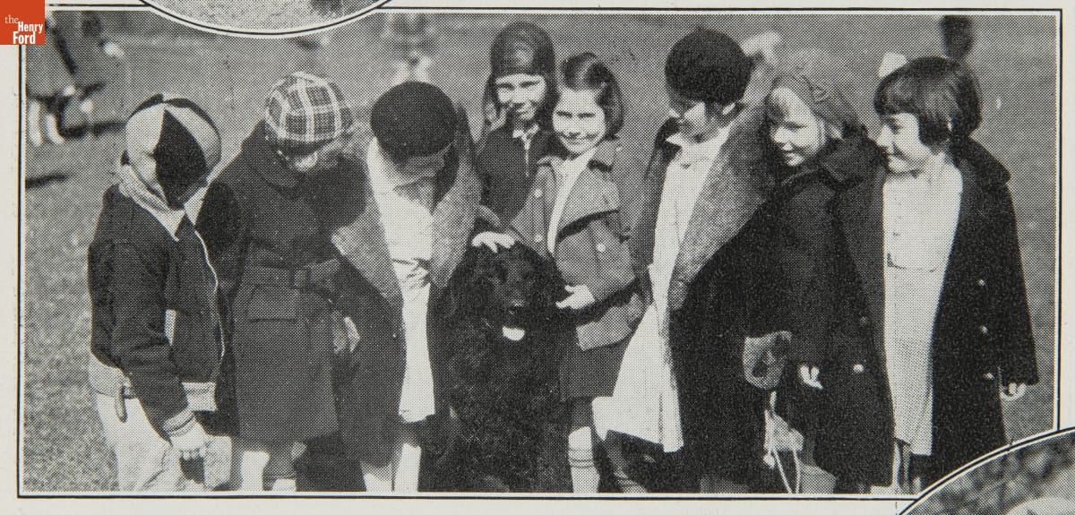 Group of children in coats gathered around seated large black dog