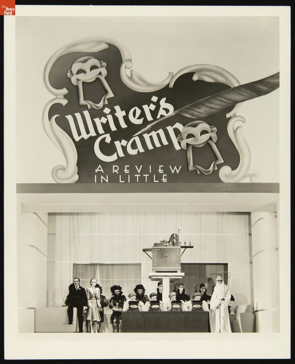 Sign with decorative edges, text, and smiling and frowning theater faces above office-themed puppet show