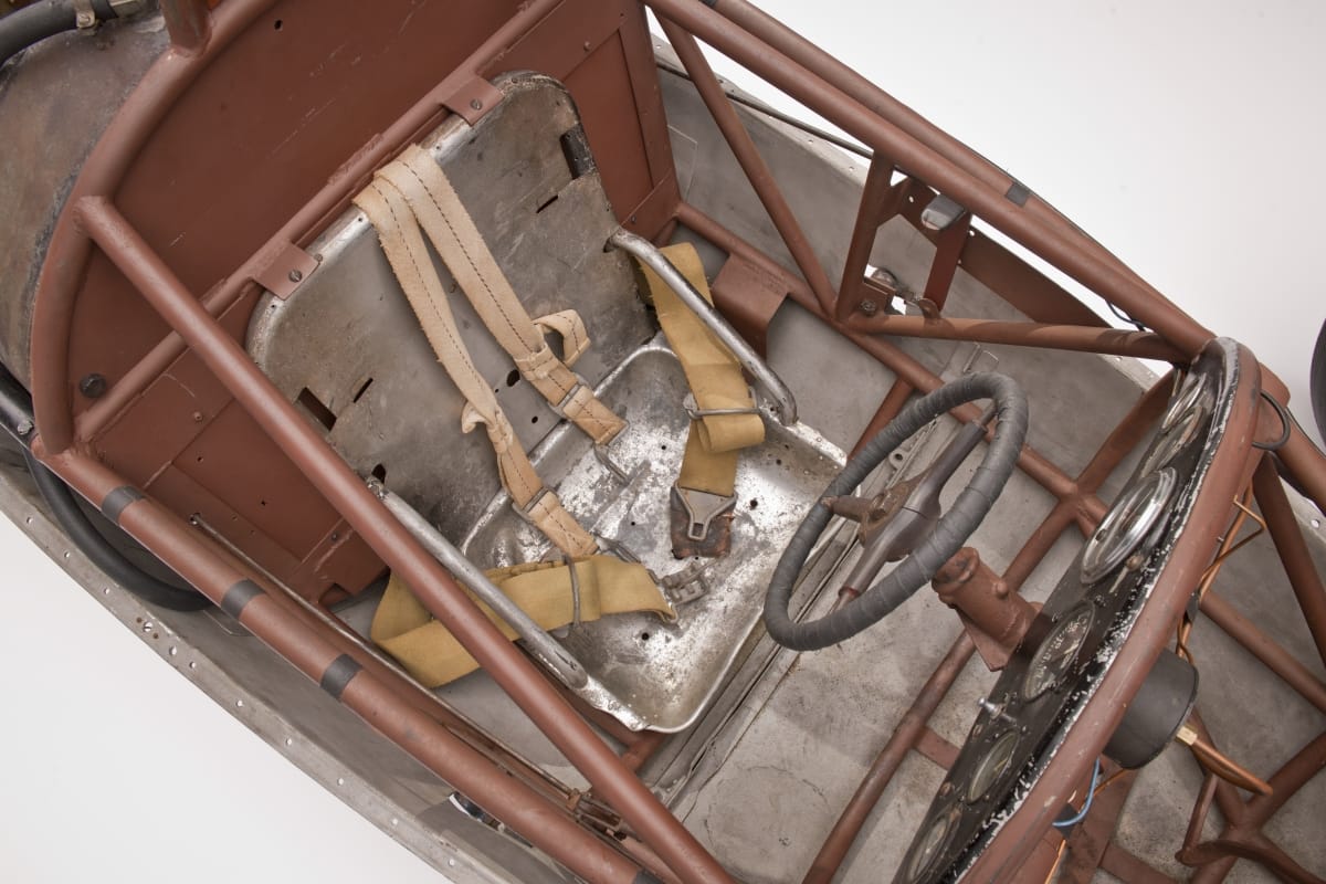 Looking down into car's open cockpit from above, with simple metal seat with harness attached