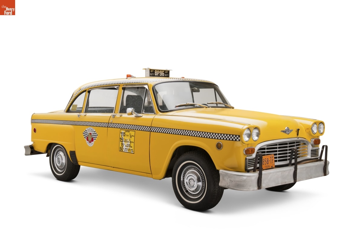Yellow taxi with signage on top and sides of car and black-and-white checked strip along full side of car