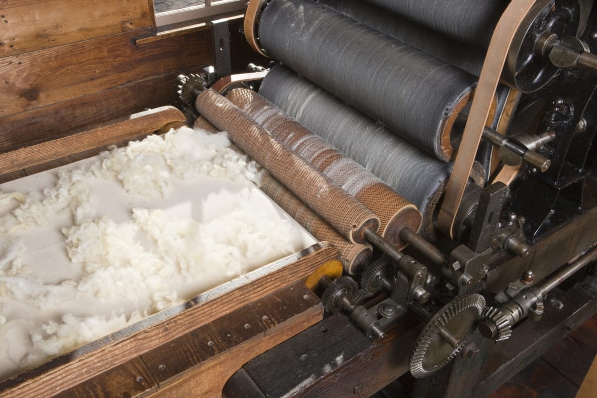 Fluffy white wool rests on a conveyor belt heading toward a machine with multiple rollers