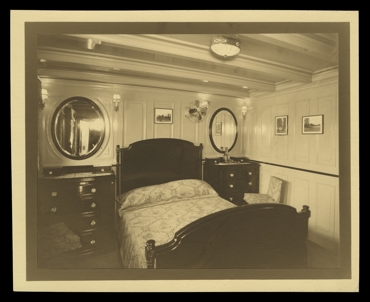 Small room containing double bed with a dresser on either side and a round mirror above each dresser