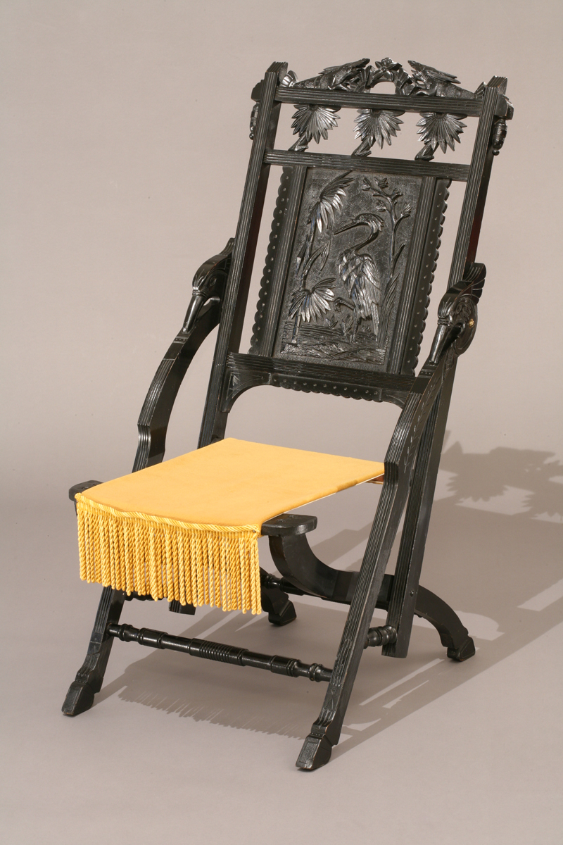 Black wooden chair with yellow tasseled seat; chair back is ornately carved with a crane and foliage