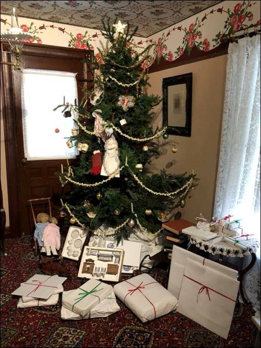 Christmas tree in the Wright Home during Holiday Nights in Greenfield Village. Decorated Christmas tree in corner of room with wrapped and unwrapped items underneath